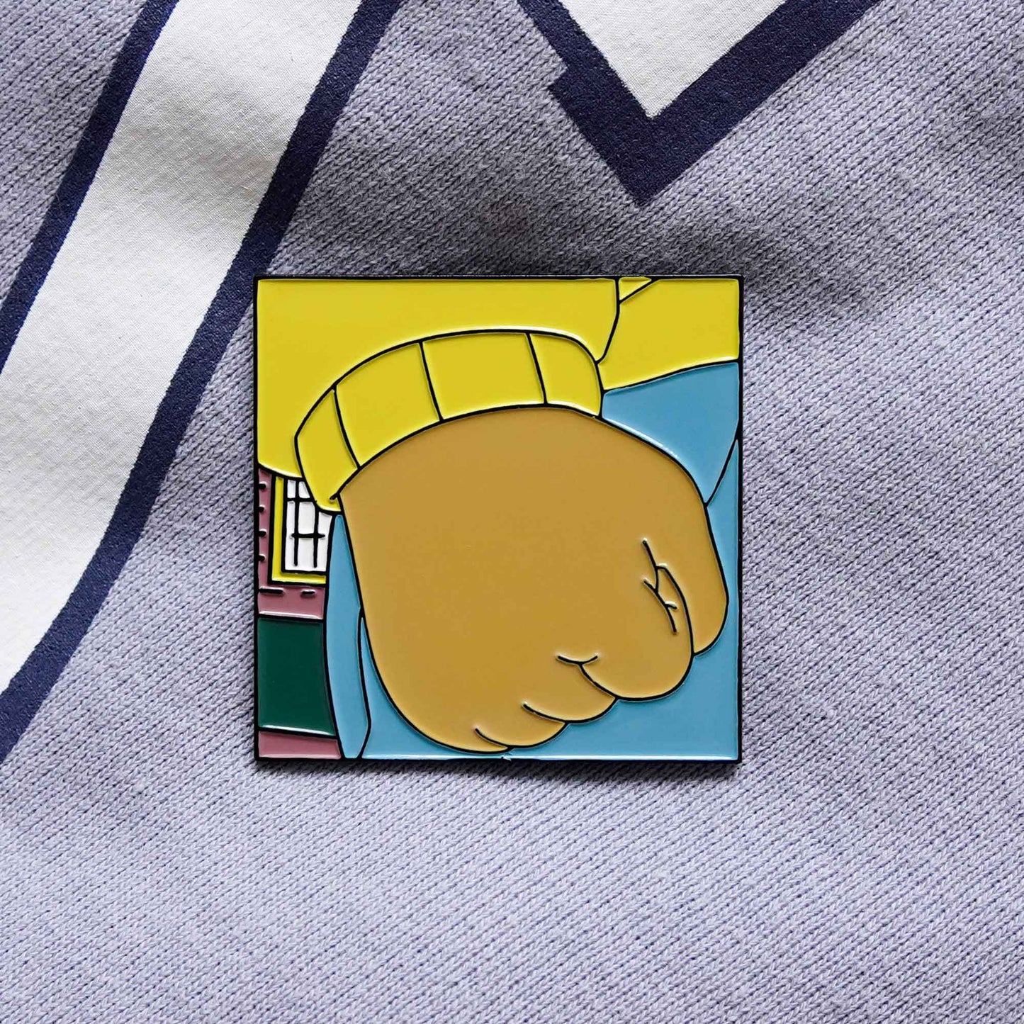 A product photo of a soft enamel pin version of the Arthur cartoon meme, where it is a close-up of his clenched fist.