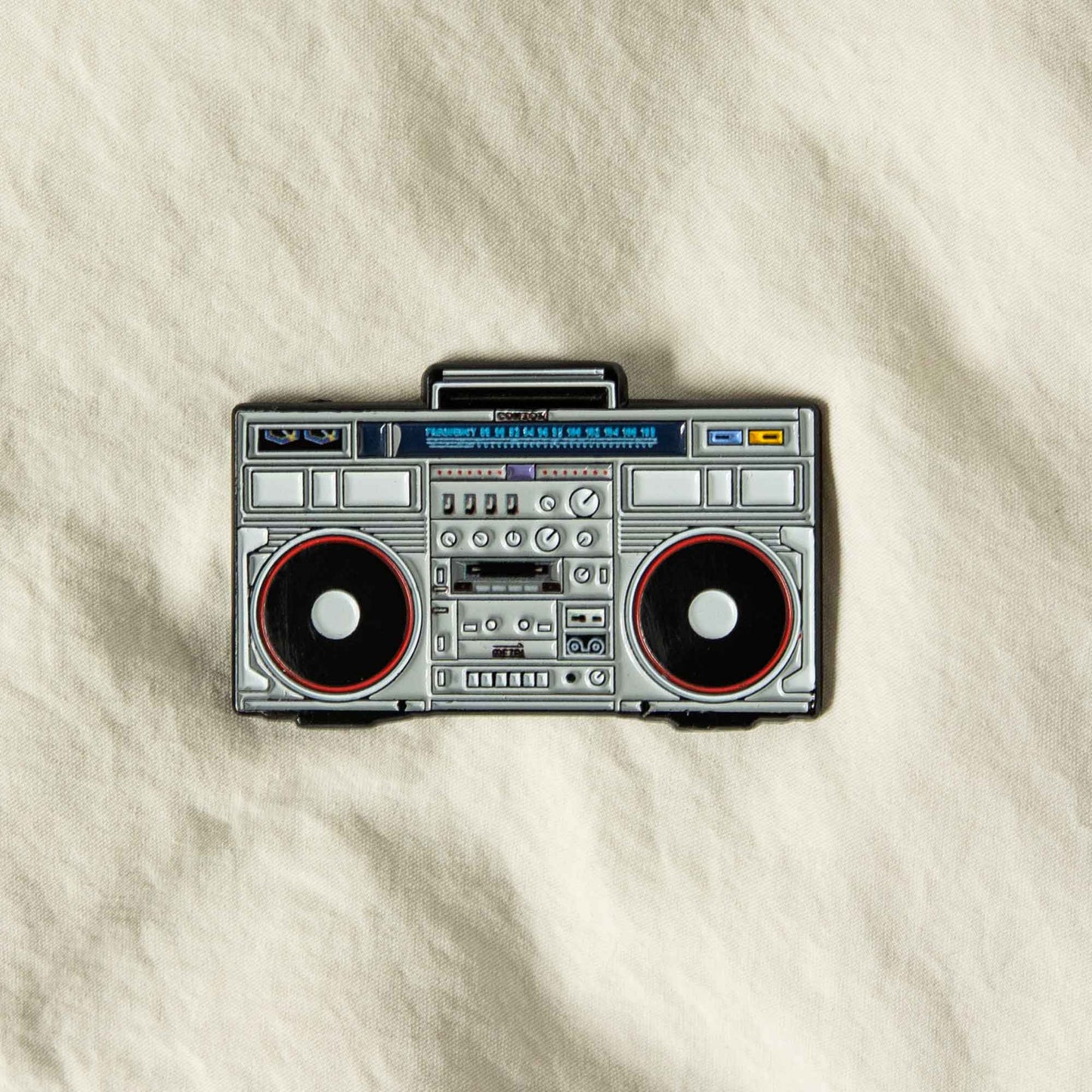 An enamel pin of a Conion Boombox C-100F.