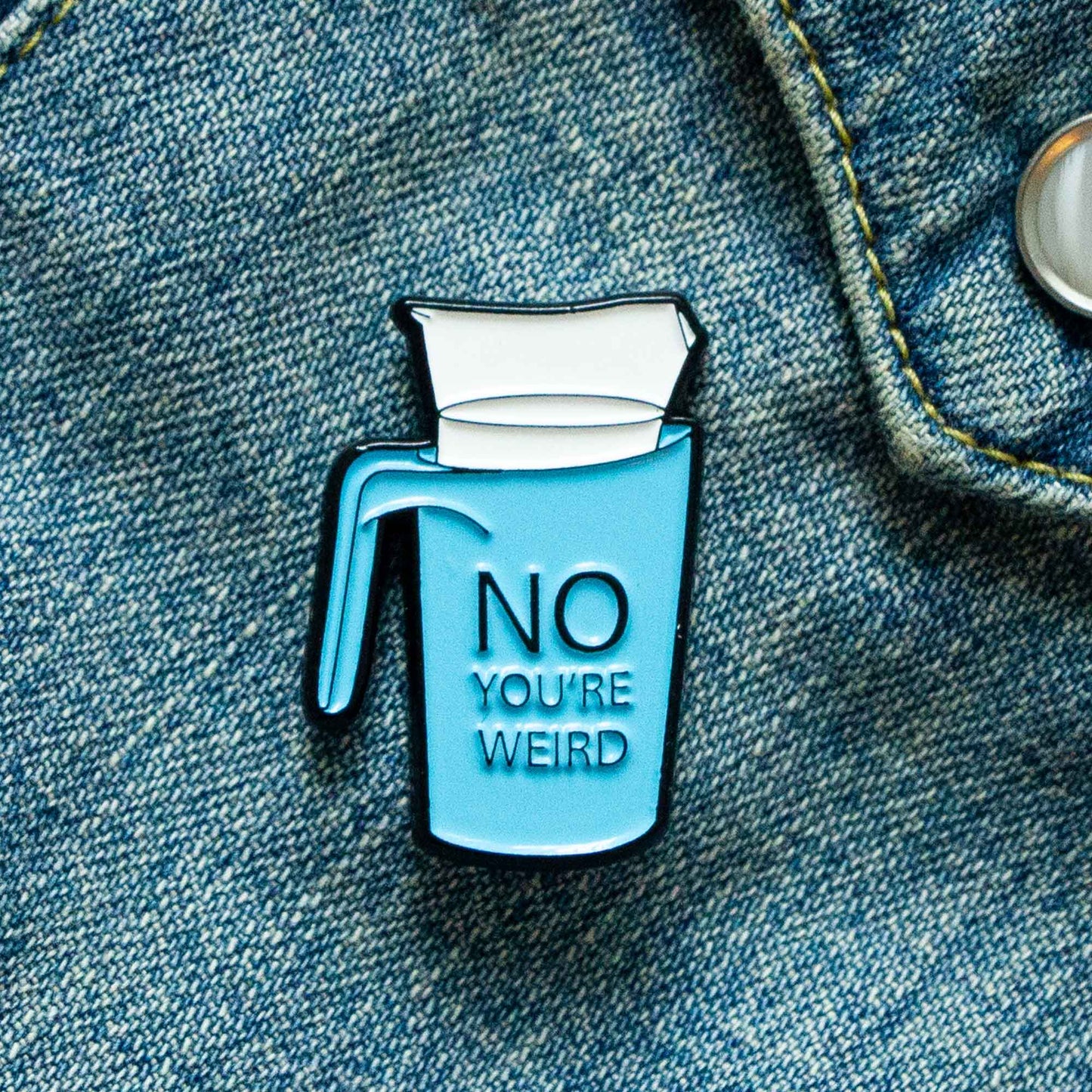 An enamel pin of a bagged milk, commonly found in Canada. The blue plastic milk container reads, "No you're weird."