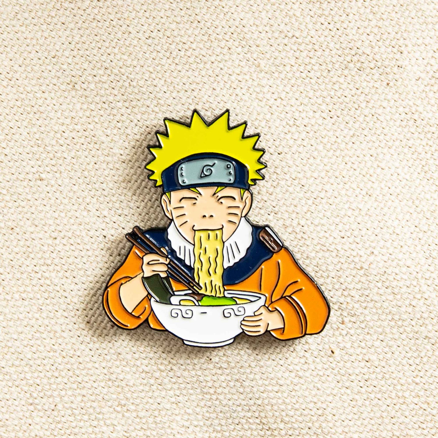 A soft enamel pin of the classic anime series, Naruto, featuring the main character, Naruto, slurping on a bowl of ramen.