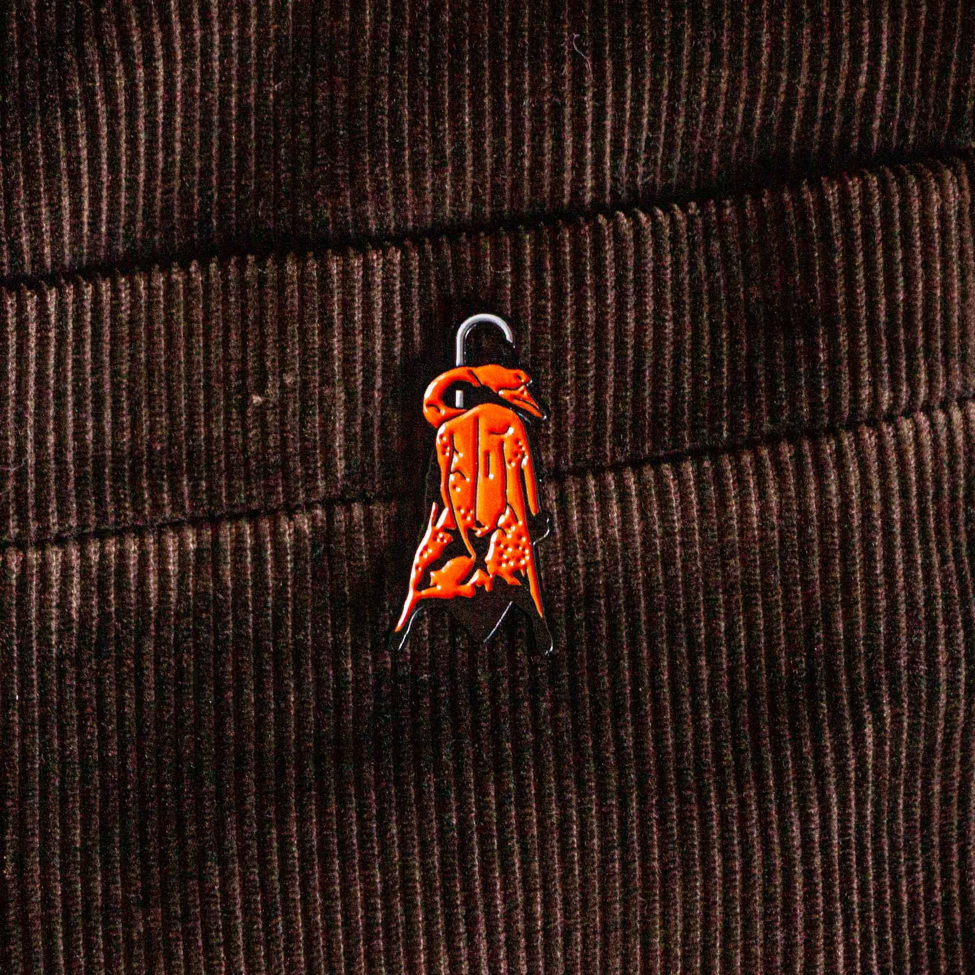 An enamel pin of a Chinese style barbecue duck hanging on a hook.