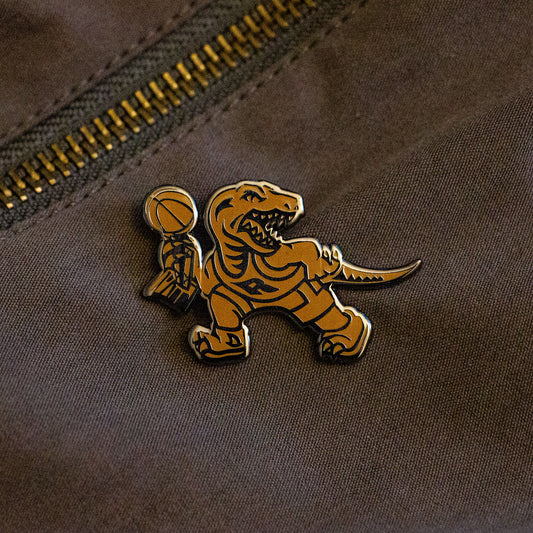 A gold hard enamel pin of the Toronto Raptors mascot logo holding the championship trophy. This design is to commemorate the NBA Championship won by the Raptors in the 2018-2019 season.