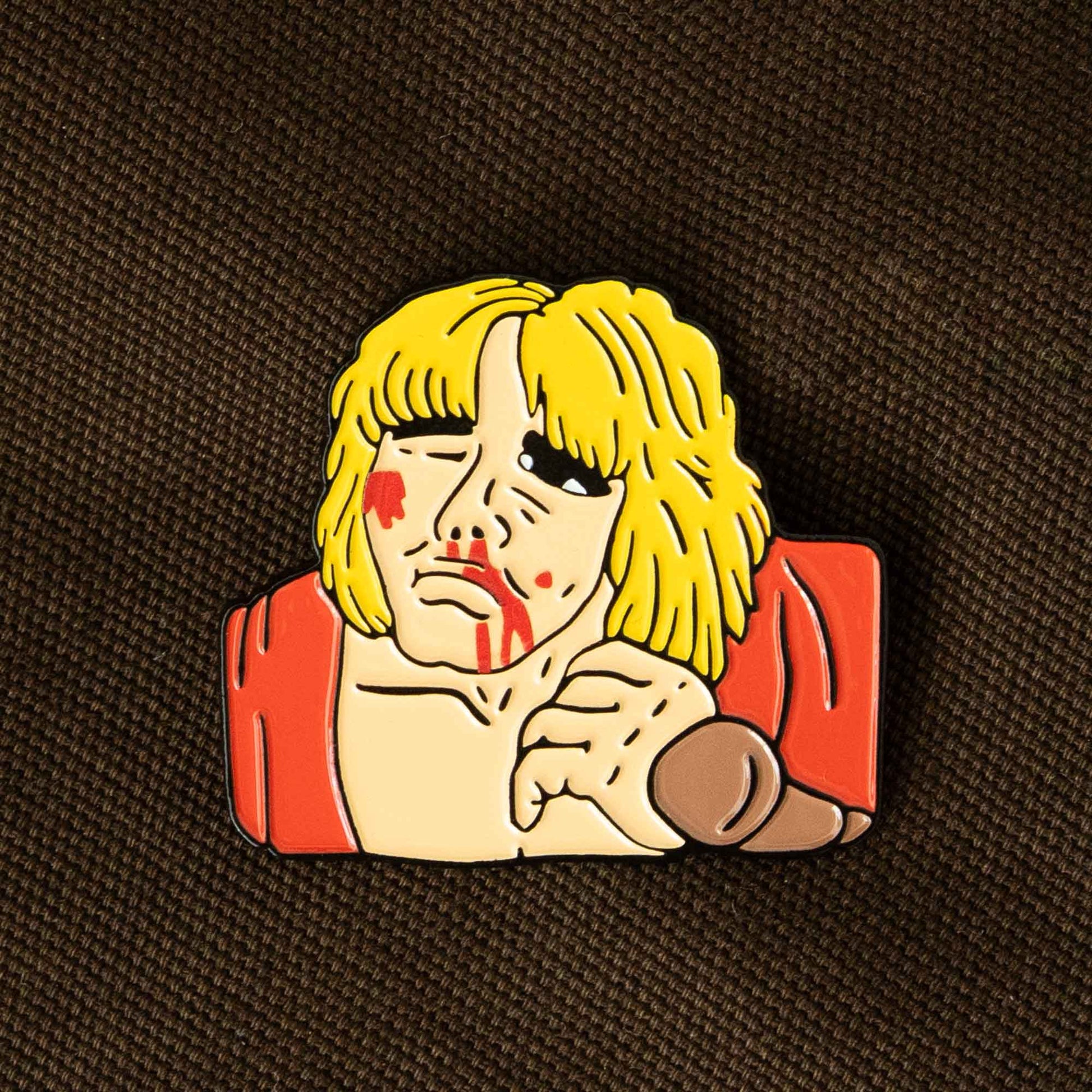 An enamel pin of the Street Fighter video game character, Ken, battered up. This pin design pays homage to the classic Street Fighter 2 game continue screen.