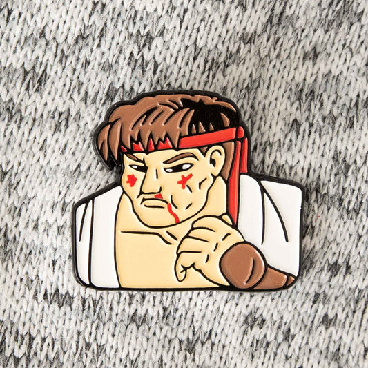 An enamel pin of the Street Fighter video game character, Ryu, battered up. This pin design pays homage to the classic Street Fighter 2 game continue screen.