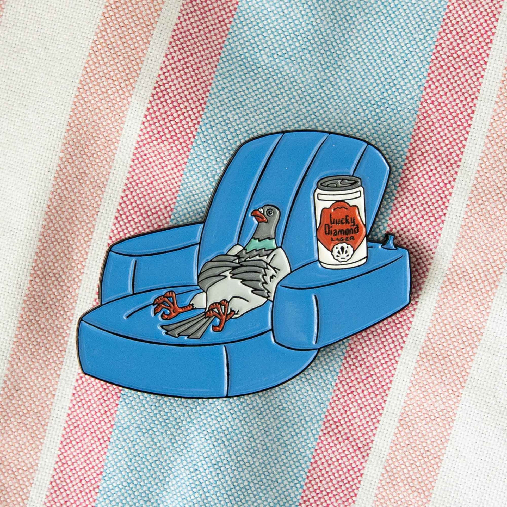 An enamel pin of Pigeon from the animated series, Mike Tyson Mysteries. He is laying on a pool floatie with a can of Lucky Diamond lager.