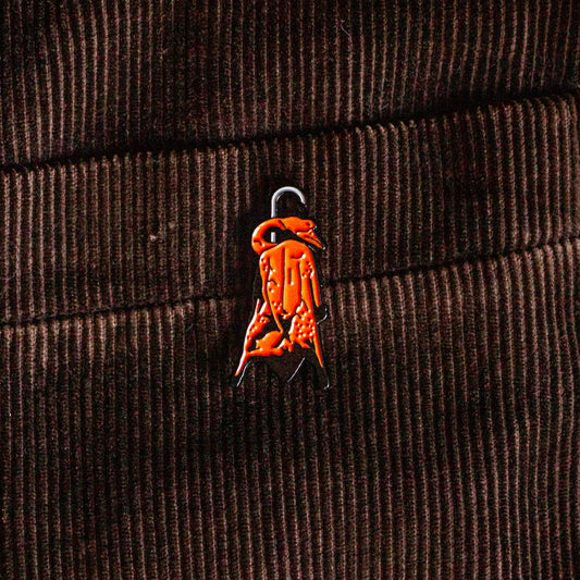 An enamel pin of a Chinese style barbecue duck hanging on a hook. 